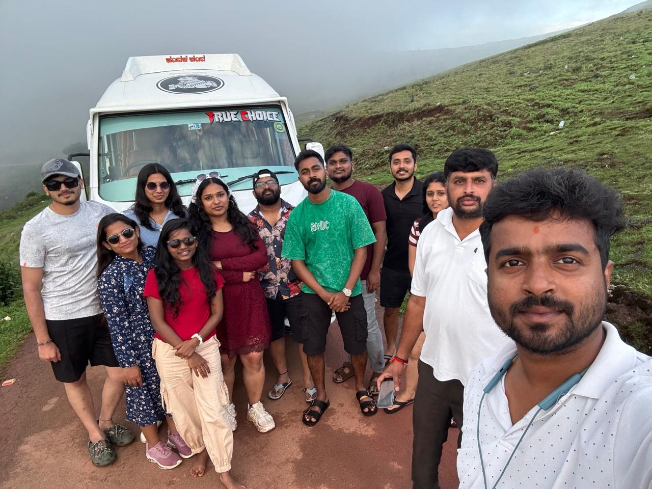 Happy family group in front of a True Choice tempo traveller on a misty Chikmagalur hilltop